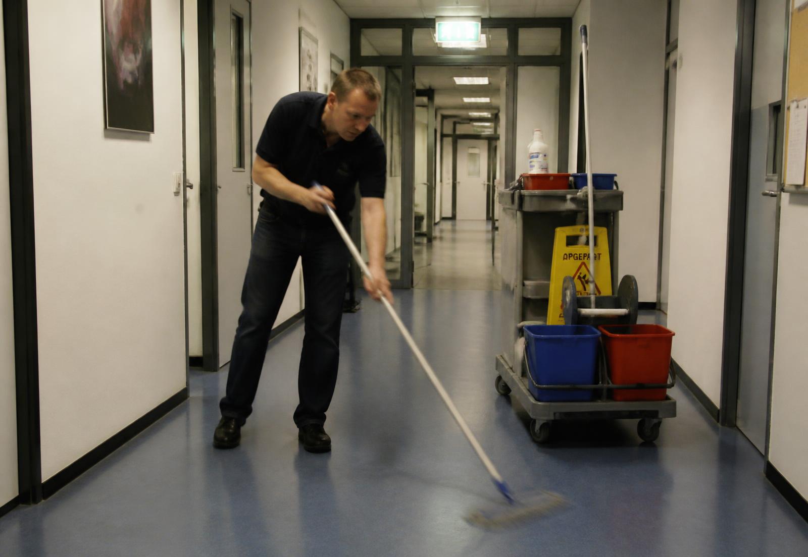 Schoonmaker dweilt een kantoorgang met schoonmaakkar